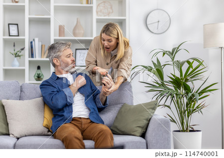Woman and man having an intense conversation after seeing a message on a smartphone while sitting on a couch. 114740001