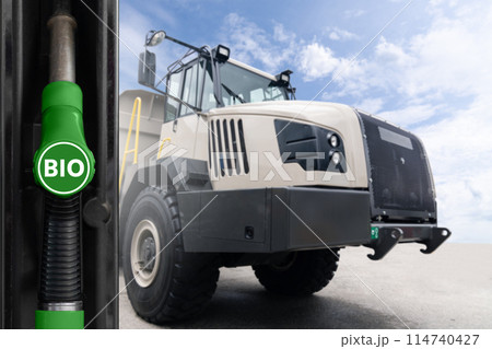Hand with biofuel filling nozzle on a background of mining truck. Decarbonization of heavy industrial vehicles Hand with biofuel filling nozzle on a background of mining truck. Decarbonization of heavy industrial vehicles 114740427