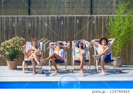 Group of cheerful seniors lying on lounge chairs by swimming pool and sunbathing. Spending hot day outdoors in backyard. 114740483