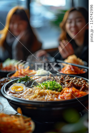 A group of Asian men and women are eating sukiyaki in a restaurant. 114742996