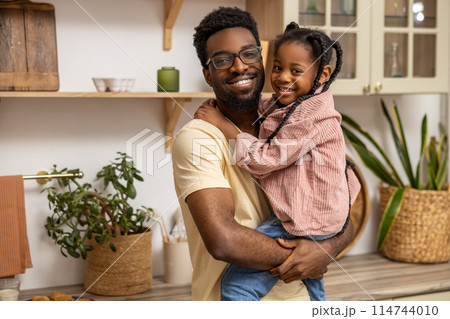 Smiling black man holding his little daughter in kitchen interior Smiling black man holding his little daughter in kitchen interior 114744010