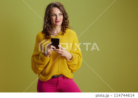 pensive fit woman in yellow sweater against green background 114744614
