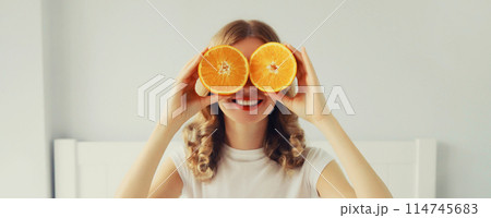 Happy healthy cheerful young woman covering her eyes with slices of orange fruits and looking for Happy healthy cheerful young woman covering her eyes with slices of orange fruits and looking for 114745683