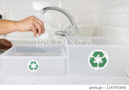 A woman washes plastic bottles in the kitchen to recycle them. A woman separates the caps from the bottles and places them in different boxes. Zero waste, eco-friendly, eco-friendly. 114745840
