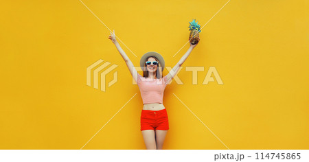 Summer cheerful young woman having fun holding pineapple, emotional girl raising her hands up 114745865