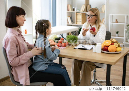 Mature woman with apple chatting with little female child and her mother. Mature woman with apple chatting with little female child and her mother. 114746042