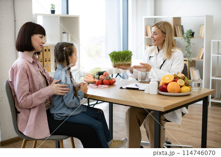 Little girl sitting on mother lap at appointment with mature female nutritionist Little girl sitting on mother lap at appointment with mature female nutritionist 114746070