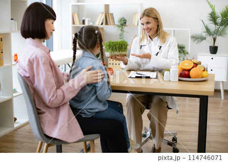 Little girl sitting on mother lap at appointment with mature female nutritionist Little girl sitting on mother lap at appointment with mature female nutritionist 114746071