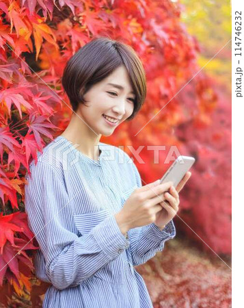 紅葉を背景にスマホをする女性 114746232