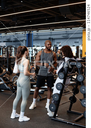 Vertical full length portrait of muscular African American man as fitness coach greeting clients in gym Vertical full length portrait of muscular African American man as fitness coach greeting clients in gym 114746524