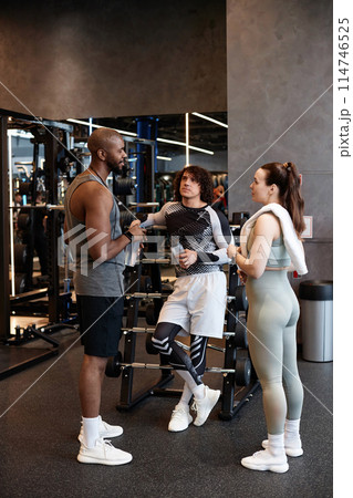 Vertical full length portrait of three sportive young people chatting in gym taking break in training 114746525