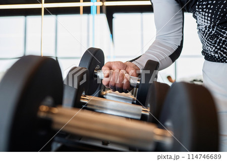 Side view closeup of muscular male hand lifting heavy dumbbell off equipment rack in gym copy space Side view closeup of muscular male hand lifting heavy dumbbell off equipment rack in gym copy space 114746689