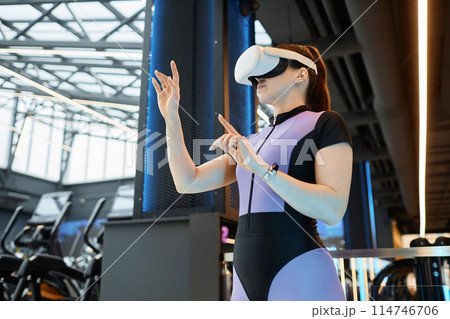 Side view portrait of young sportswoman wearing VR headset in futuristic gym training and using interactive hand tracking copy space 114746706