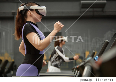 Side view portrait of sportive woman running on treadmill with VR headset during immersive workout session 114746744