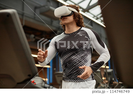 Waist up portrait of sportive young man wearing VR headset running on treadmill in gym during immersive training session copy space Waist up portrait of sportive young man wearing VR headset running on treadmill in gym during immersive training session copy space 114746749