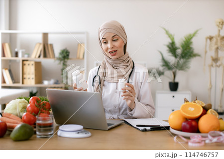 Positive arabian nutritionist woman holding pills or vitamins in hands. Positive arabian nutritionist woman holding pills or vitamins in hands. 114746757