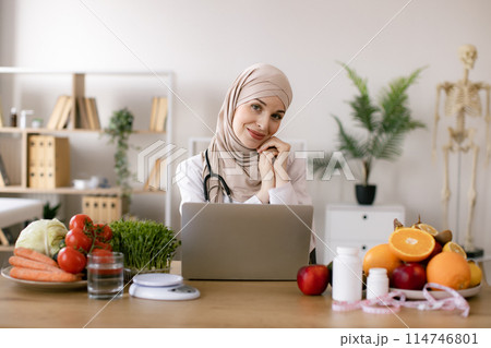 Nutritionist working on laptop and writing diet plan for patient. Nutritionist working on laptop and writing diet plan for patient. 114746801