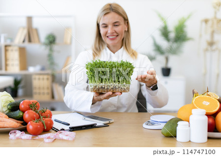 Charming Caucasian woman in doctor's coat with microgreens. Charming Caucasian woman in doctor's coat with microgreens. 114747100