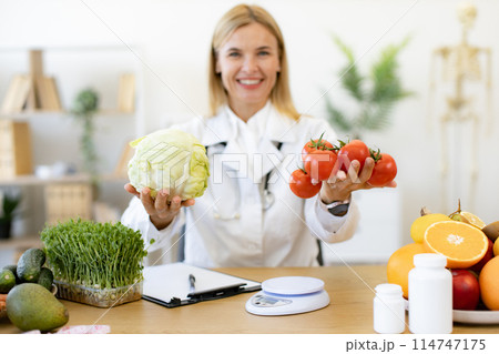 Mature female doctor nutritionist holds fresh organic tomatoes and cabbage. Mature female doctor nutritionist holds fresh organic tomatoes and cabbage. 114747175