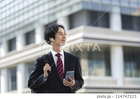 イヤホンをつけてスマートフォンを持った30代のビジネスマン 114747223