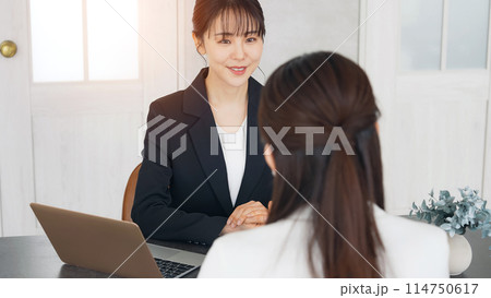 オフィスで会話する二人のビジネスウーマン オフィスで会話する二人のビジネスウーマン 114750617