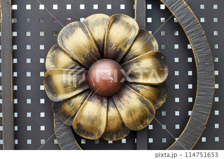 Close-up detail of beautiful vintage forged metal big yellow and red flower decorating iron gray fence, gate or door. Work of blacksmith, protection, art and fantasy concept. 114751653