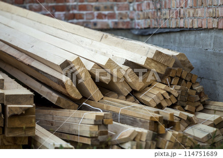 Close-up of piled stack of natural brown uneven rough wooden boards lit by bright sun. Industrial timber for carpentry, building, repairing and furniture, lumber material for construction. 114751689