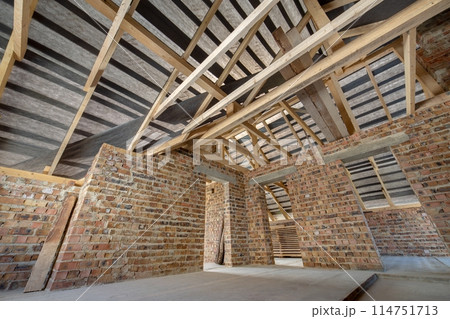 Attic of a building under construction with wooden beams of a roof structure and brick walls. Attic of a building under construction with wooden beams of a roof structure and brick walls. 114751713