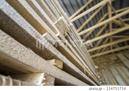 Neatly piled long stack of wooden boards inside attic room under construction. 114751714