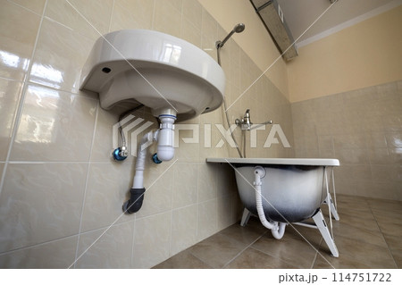 Bottom view of new white washbasin sink connected to sewer on background of bathroom light beige ceramic tiles. Professional plumbing and installation concept. Bottom view of new white washbasin sink connected to sewer on background of bathroom light beige ceramic tiles. Professional plumbing and installation concept. 114751722