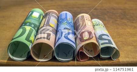 Five, ten, twenty, fifty and one hundred euro rolled bills banknotes on wooden table background. Five, ten, twenty, fifty and one hundred euro rolled bills banknotes on wooden table background. 114751961
