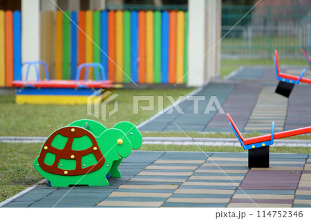 Bright colorful funny bench on nursery playground with soft rubber flooring on bright sunny summer day. Children activities and recreation outdoors. Bright colorful funny bench on nursery playground with soft rubber flooring on bright sunny summer day. Children activities and recreation outdoors. 114752346