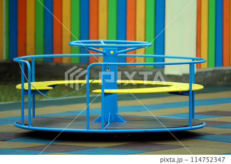 Beautiful playground in kindergarten with soft pavement, bright swings, roundabout and bench on sunny day. Perfect place for children activities outdoors. Beautiful playground in kindergarten with soft pavement, bright swings, roundabout and bench on sunny day. Perfect place for children activities outdoors. 114752347