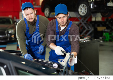 Two professional auto mechanics repairing broken car together in car service center Two professional auto mechanics repairing broken car together in car service center 114753168