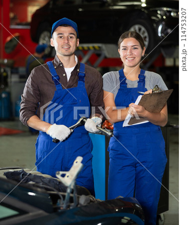 Portrait of two auto mechanics - man and girl against the background of cars in car service center 114753207