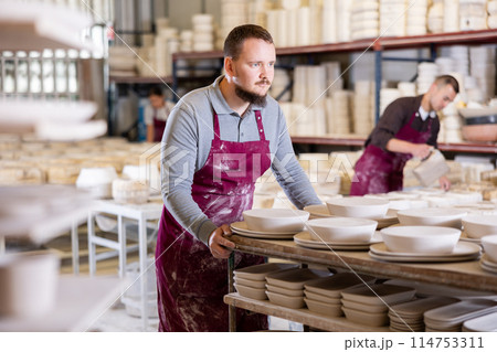 Young man moves rack with ceramic blanks Young man moves rack with ceramic blanks 114753311