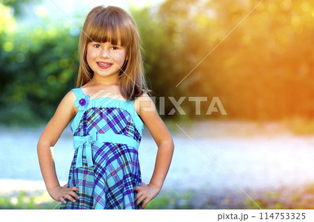 Outdoor portrait of optimistic smiling pretty little girl in blue dress 114753325