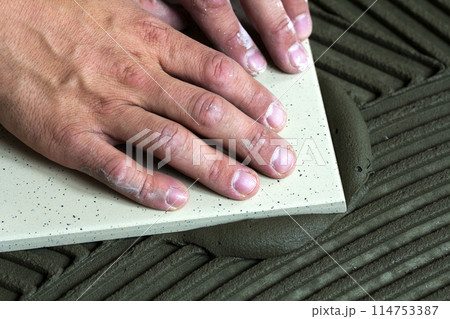 Ceramic tiles and tools for tiler. Worker hand installing floor tiles. Home improvement, renovation - ceramic tile floor adhesive, mortar, level. 114753387