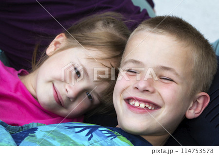 Close-up portrait of two small cute blond happily smiling children, brother and sister, boy and girl laying in bed under colorful blanket. Careless innocent childhood and siblings friendship concept. 114753578