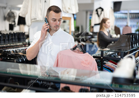 While shopping, man chooses gift, examines womans blouse and talks on phone 114753595