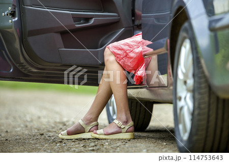 Young woman in short dress getting out car with open door on sunny blurred rural road background. Young woman in short dress getting out car with open door on sunny blurred rural road background. 114753643