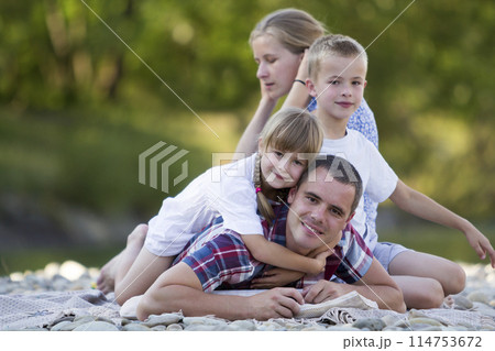 Family portrait of young happy mother, father and two cute blond children, boy and girl on bright summer day with green bokeh background. Happy family relations, love, care and perfect holiday concept 114753672