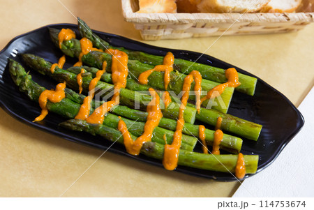 Steamed asparagus under romesk sauce on a black plate 114753674