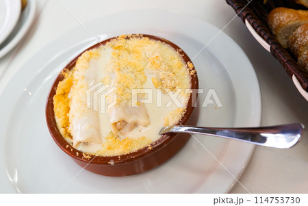 Appetizing Spanish style baked cannelloni filled with meat in cream sauce served in pottery 114753730