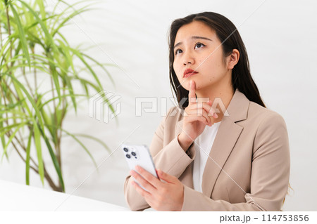 ビジネススーツを着てスマートフォンをしている若い女性 ビジネスイメージ ビジネススーツを着てスマートフォンをしている若い女性 ビジネスイメージ 114753856