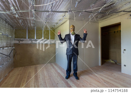 Strange man in businessman suit and gas protection mask inside a room under renovation works. 114754188
