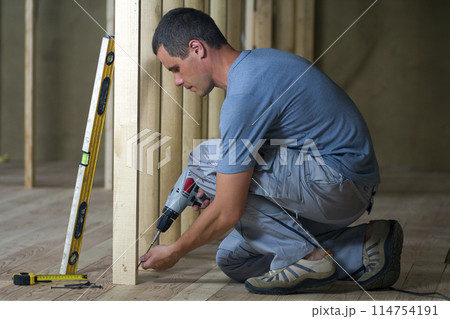 Young professional worker uses level and screwdriver installing wooden frame for future walls. Interior of attic insulated room with oak floor under reconstruction. Renovation and improvement concept. 114754191