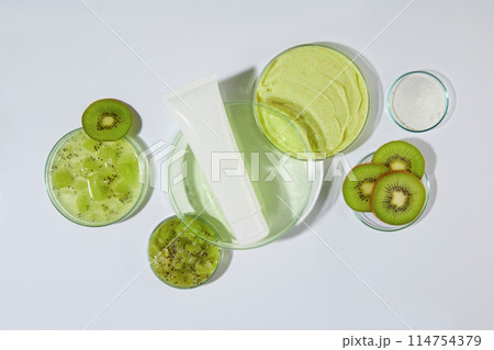 Photograph for exfoliating cream has kiwi ingredient advertising , a blank scrubs tube displayed on a glass dish with a little light green liquid, white background. High angle shot, space for text Photograph for exfoliating cream has kiwi ingredient advertising , a blank scrubs tube displayed on a glass dish with a little light green liquid, white background. High angle shot, space for text 114754379