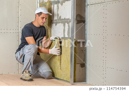 Worker insulating a room wall with mineral rock wool thermal insulation. 114754394