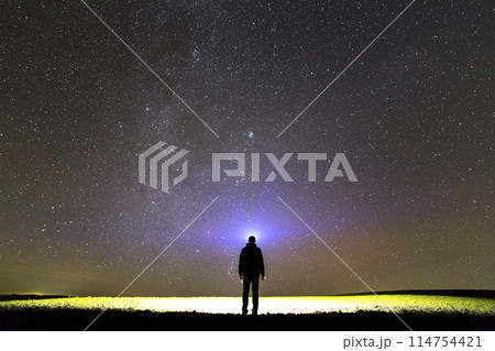Black silhouette of man with head flashlight on grassy field under beautiful dark summer starry sky. Black silhouette of man with head flashlight on grassy field under beautiful dark summer starry sky. 114754421